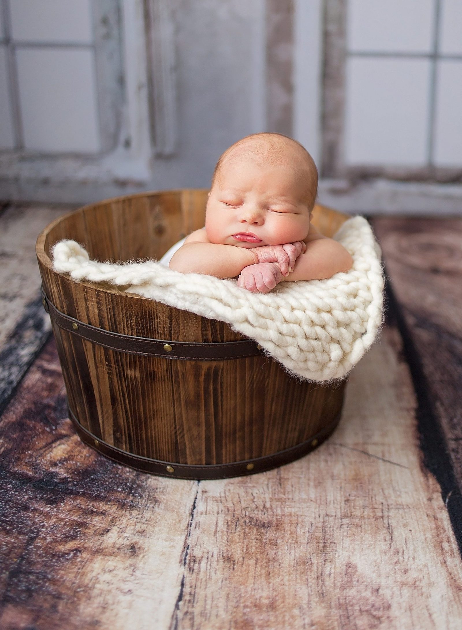Newborn baby boy in a bucket with a cream blanket