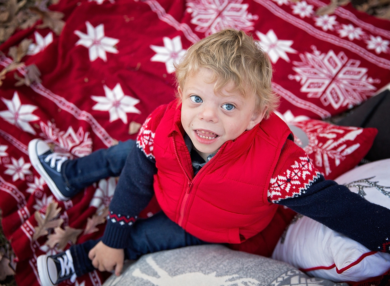 Special Needs Boy in red vest and blue jeans sitting on red blanket