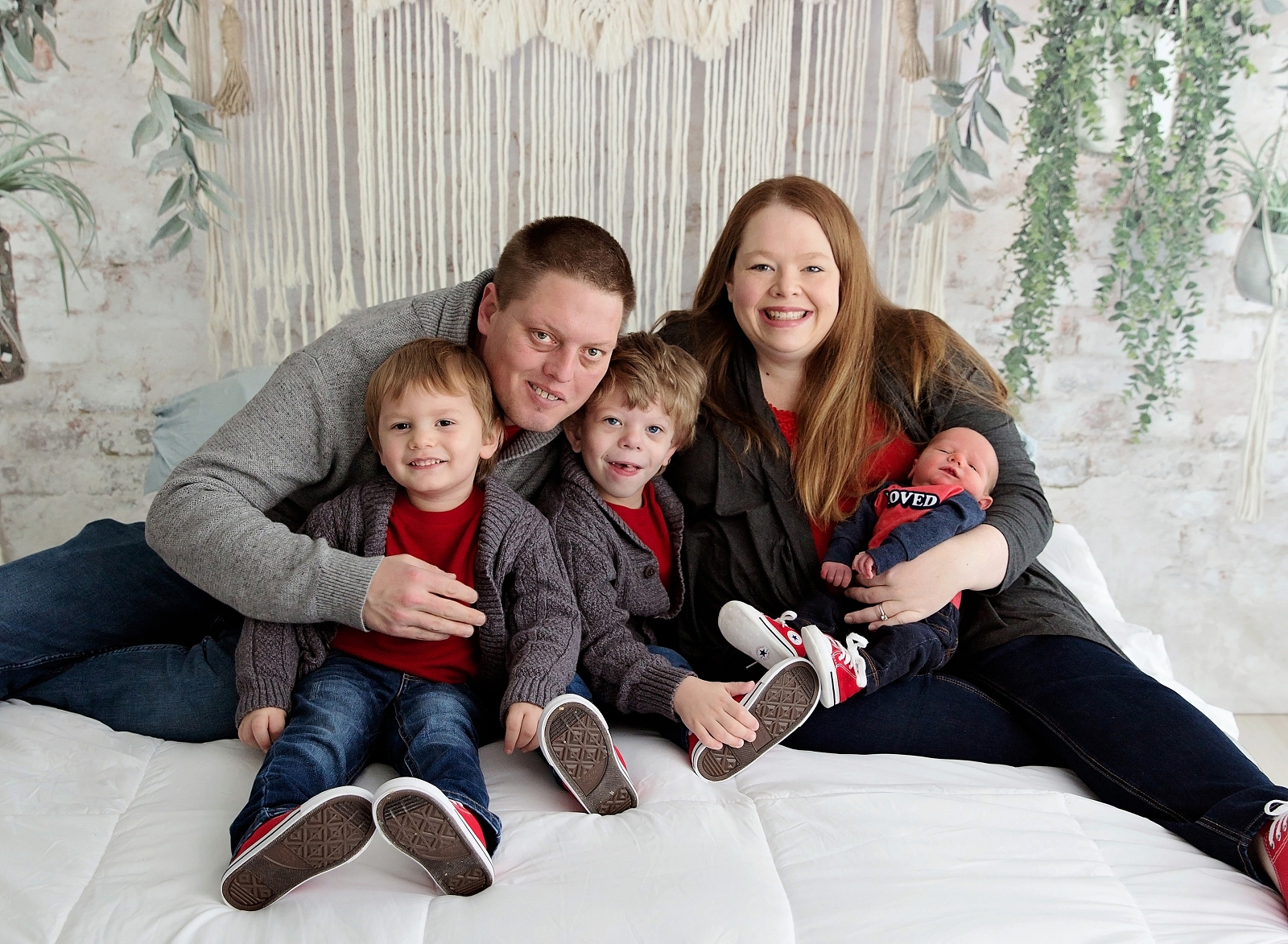 Family with three boys in red on a bed.